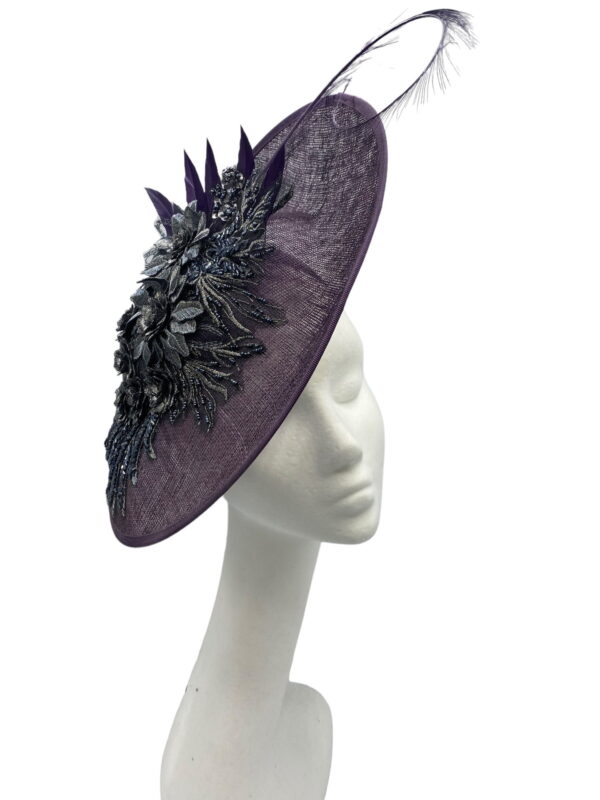 Purple saucer style headpiece with pewter embellishment to the side finished with a spray of colour matching feathers.